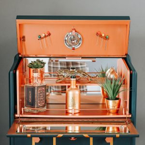 Art Deco cocktail cabinet copper interior with mirrored shelf and bar accessories.